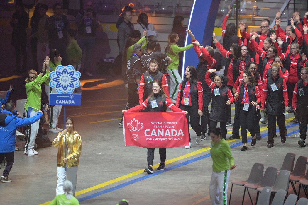 Groupe d'athlètes entrant dans la cérémonie d'ouverture. L'athlète de devant tient une bannière canadienne avec les mots « Équipe Canada des Olympiques spéciaux ». Tous les athlètes sont vêtus de rouge et de noir.