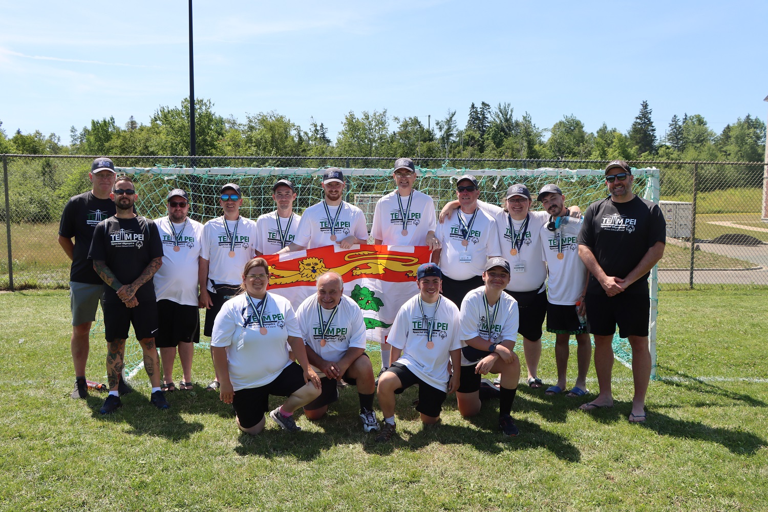 Team PEI 2026 athletes and coaches standing on the field, with their medals and the PEI flag