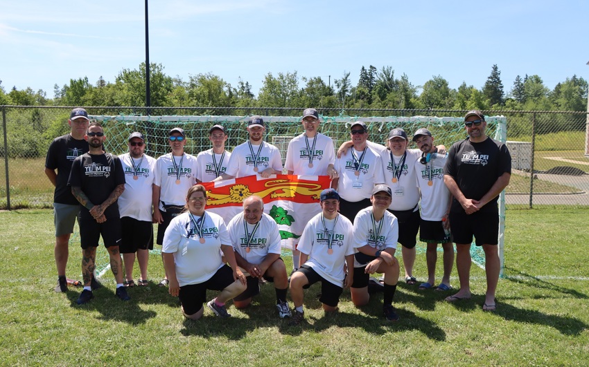 Team PEI 2026 athletes and coaches standing on the field, with their medals and the PEI flag