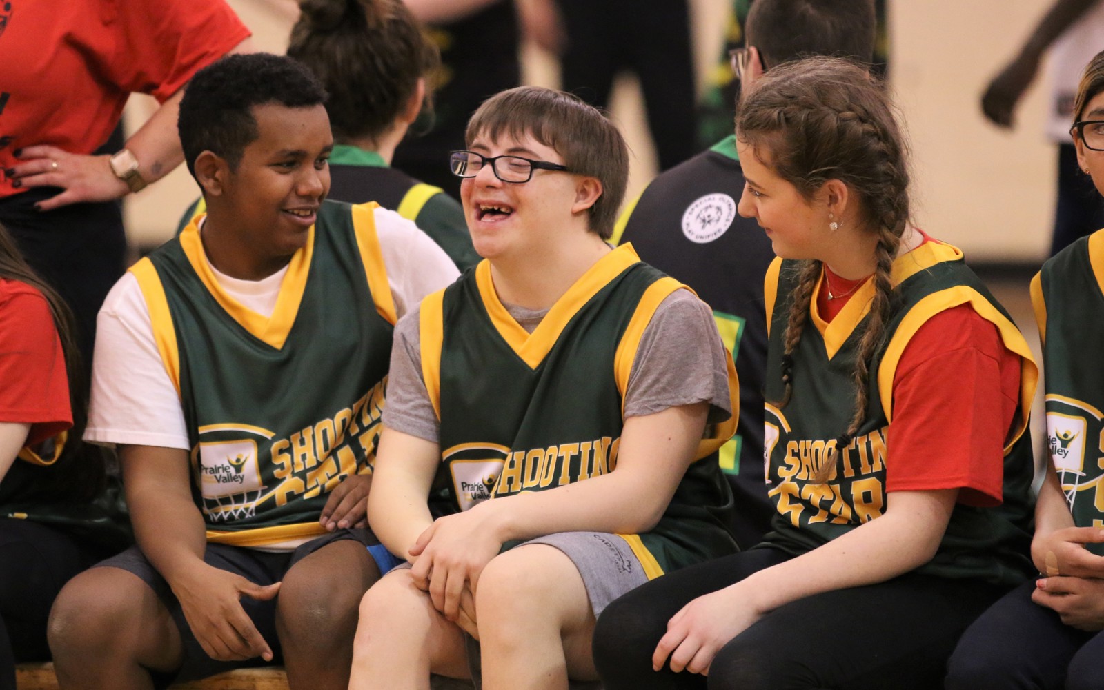 Three basketball athletes sitting on the bench. They are all talking with each other and smiling and laughing.