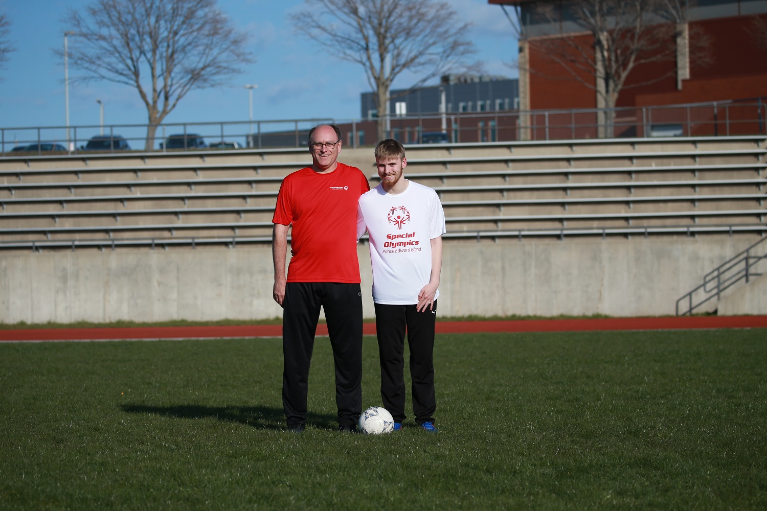 An athlete and a volunteer stand together outside on a soccer field
