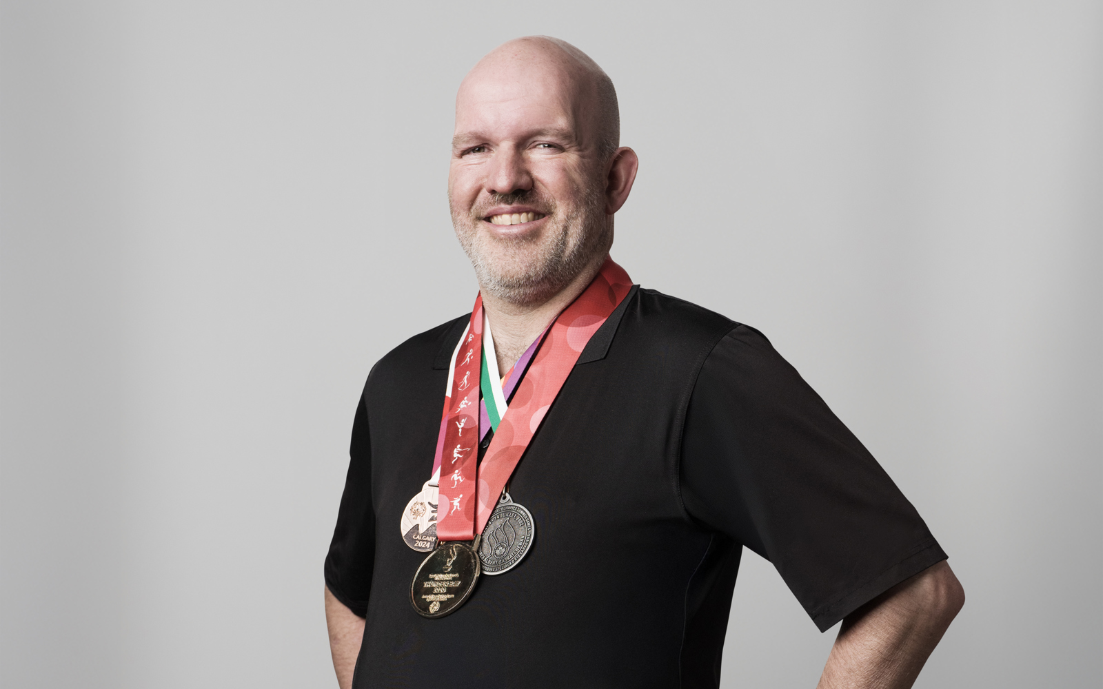 Older man in all black wearing medals around his neck. 