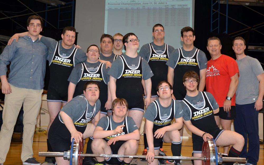 A Special Olympics Newfoundland & Labrador powerlifting team group photo. Everyone is standing in a gym in front of a large dumbbell.