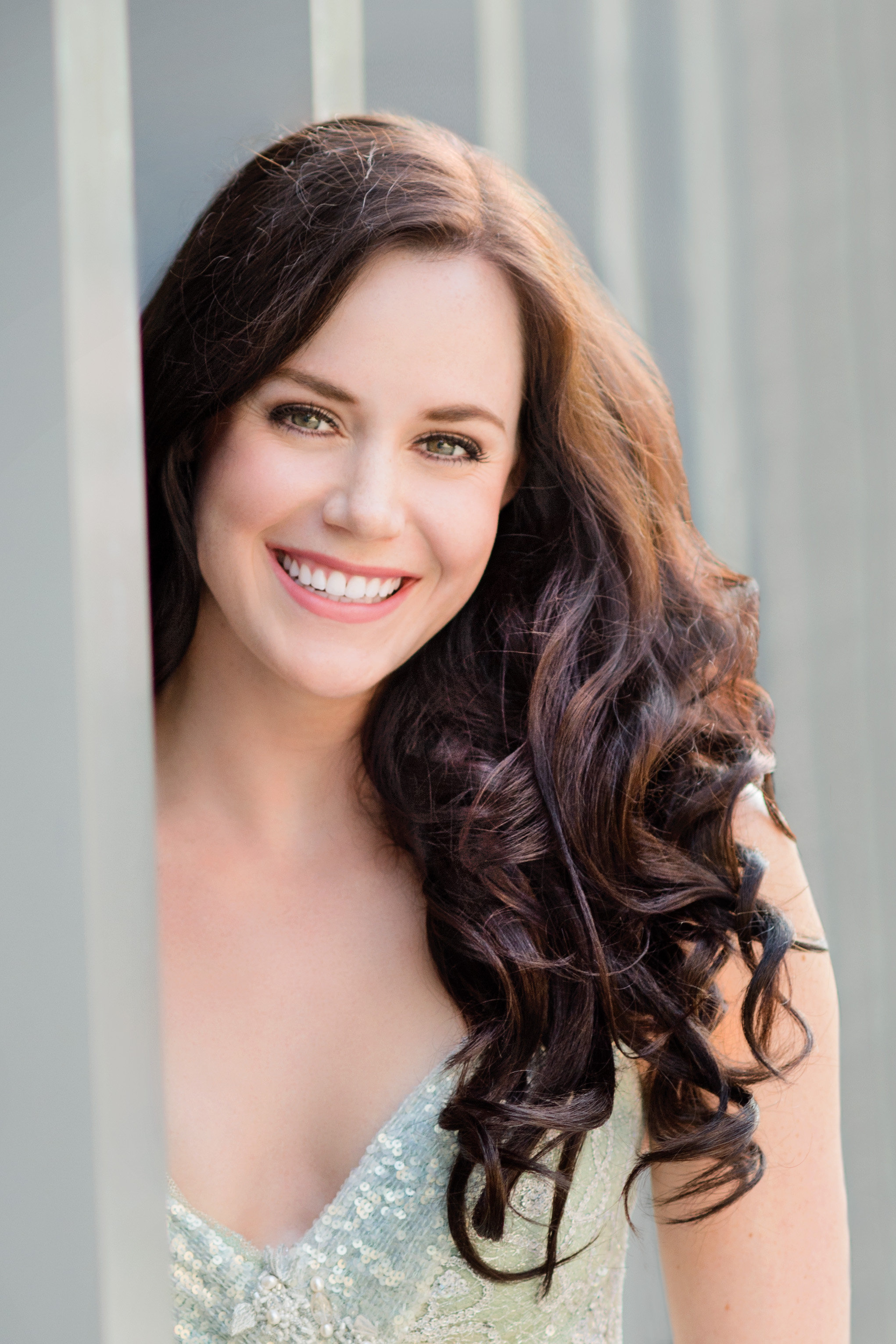 Headshot of a woman with dark culy hair wearing a pale green sequined top. Headshot of a woman with dark culy hair wearing a pale green sequined top.