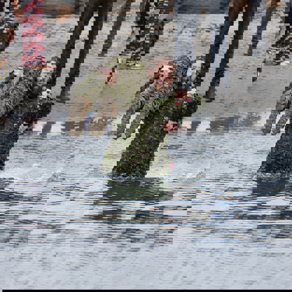 A Law Enforcement Torch Run Polar Plunge participant carries another participant on their shoulder as they enter the water.