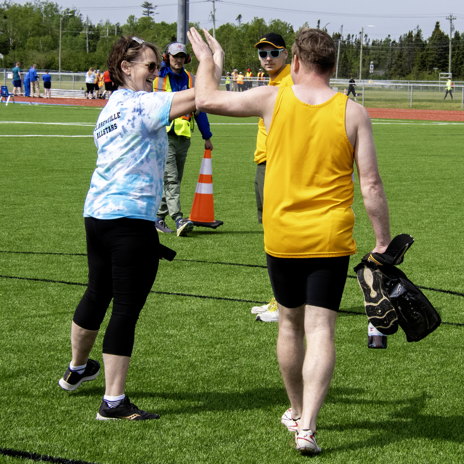 A coach is giving a high-five to an athlete. The photo was taken from behind the pair and you can only see a glimpse of the coach's face, smiling at the athlete. The athlete is holding his equipment in the hand not being used for the high five.