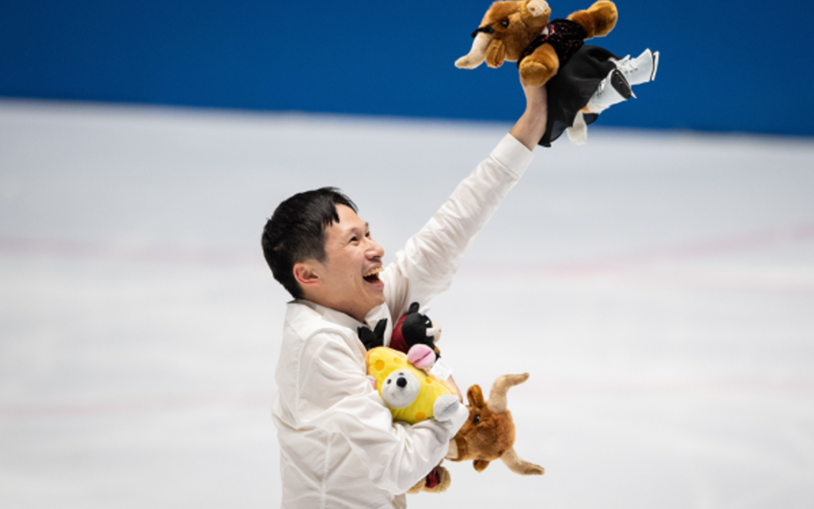 Young person in a white shirt holds up stuffed animals. They are on an ice rink. 