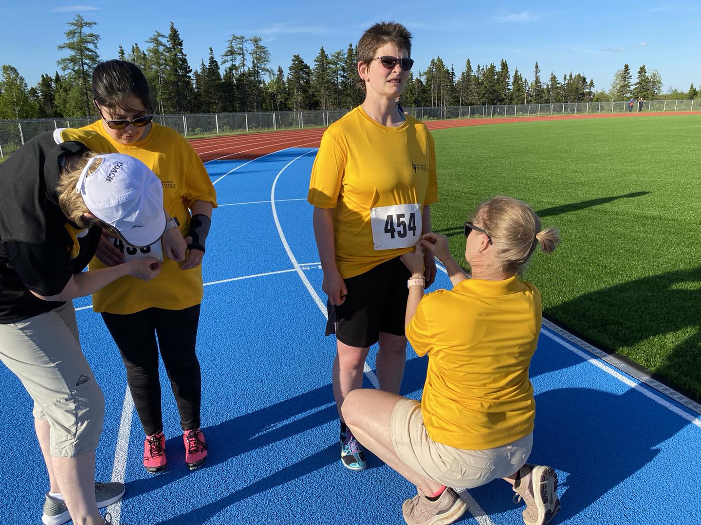 Two athletes in yellow shirts having competition bibs pinned on them by volunteers on a race track. Two athletes in yellow shirts having competition bibs pinned on them by volunteers on a race track.