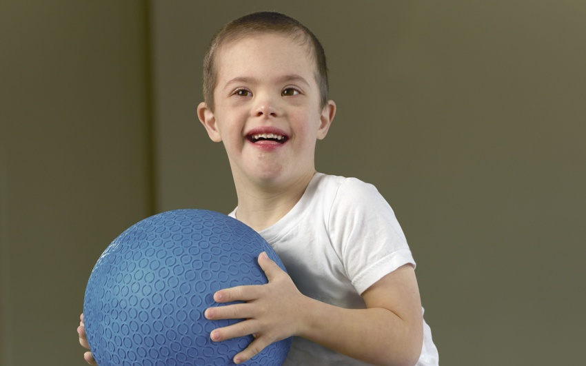 Toddler boy in a white shirt and black shorts holding a blue ball 