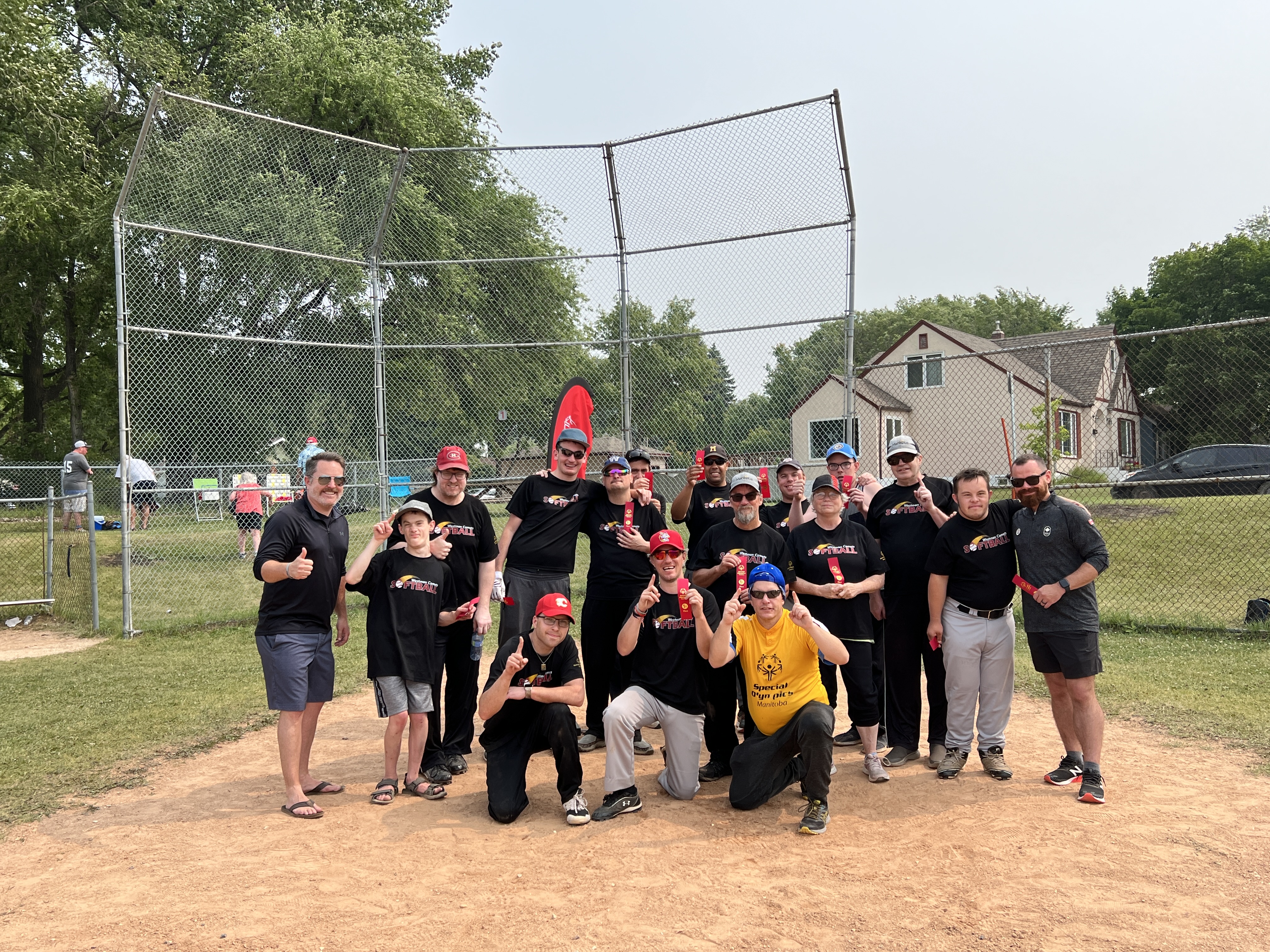 Photo of a diverse group of people all dressed in black shirts on a baseball diamond. 