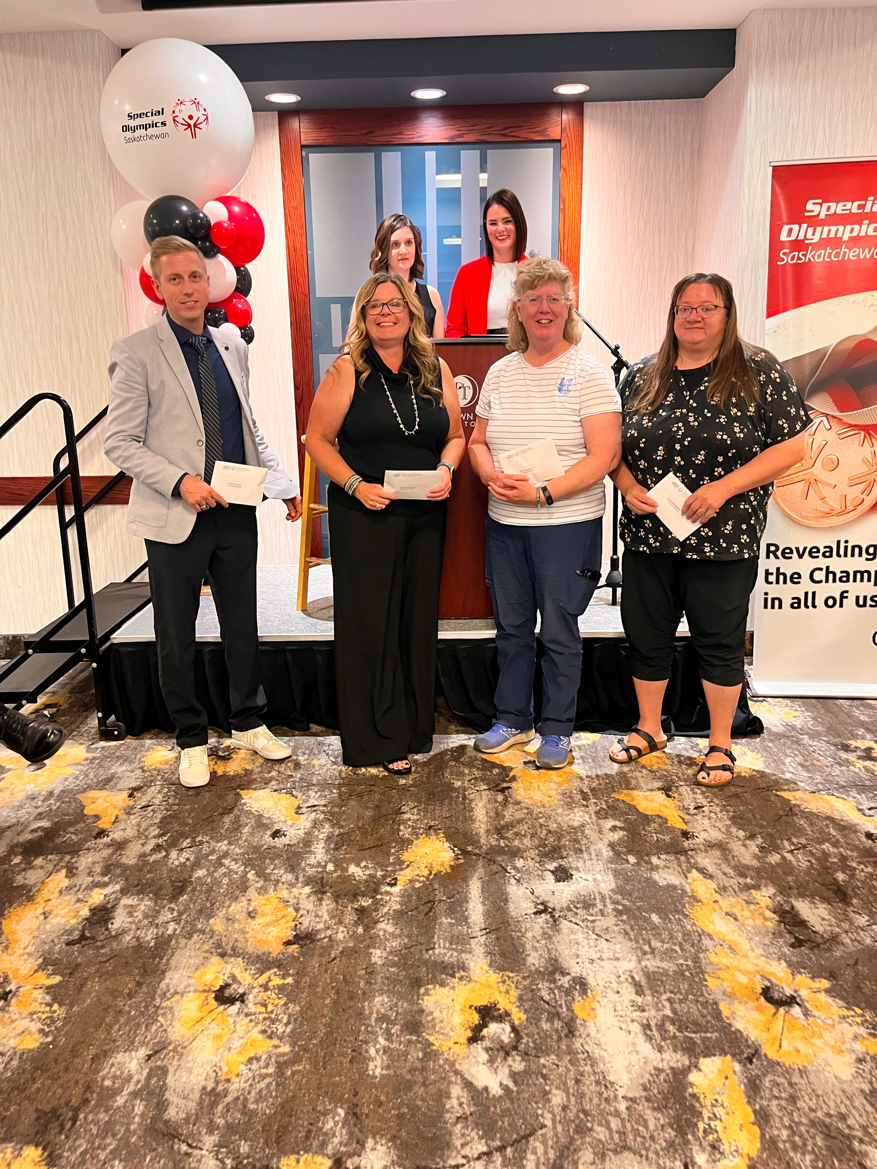 Four individuals are standing in front of a podium and holding out the awards they just won. They are smiling and posing for the camera. Four individuals are standing in front of a podium and holding out the awards they just won. They are smiling and posing for the camera.