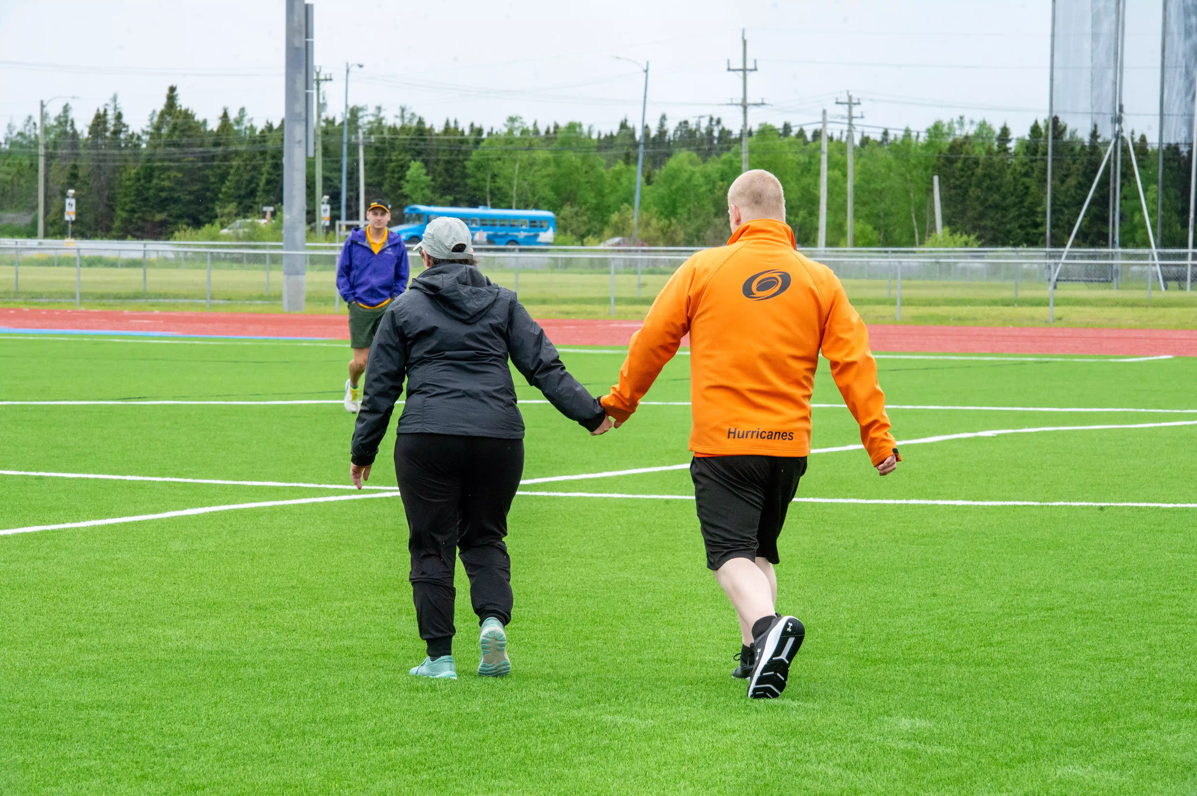Two athletes holding hands walking on the field. The photo was captured from behind the athletes so you cannot see their faces. They are both wearing light rain jackets to prepare for the weather. Two athletes holding hands walking on the field. The photo was captured from behind the athletes so you cannot see their faces. They are both wearing light rain jackets to prepare for the weather.