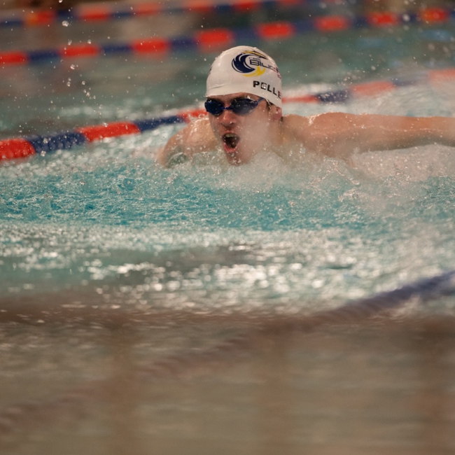 An action shot photo of a swimming athlete in the water. The athlete is wearing black goggles and a white swim cap.