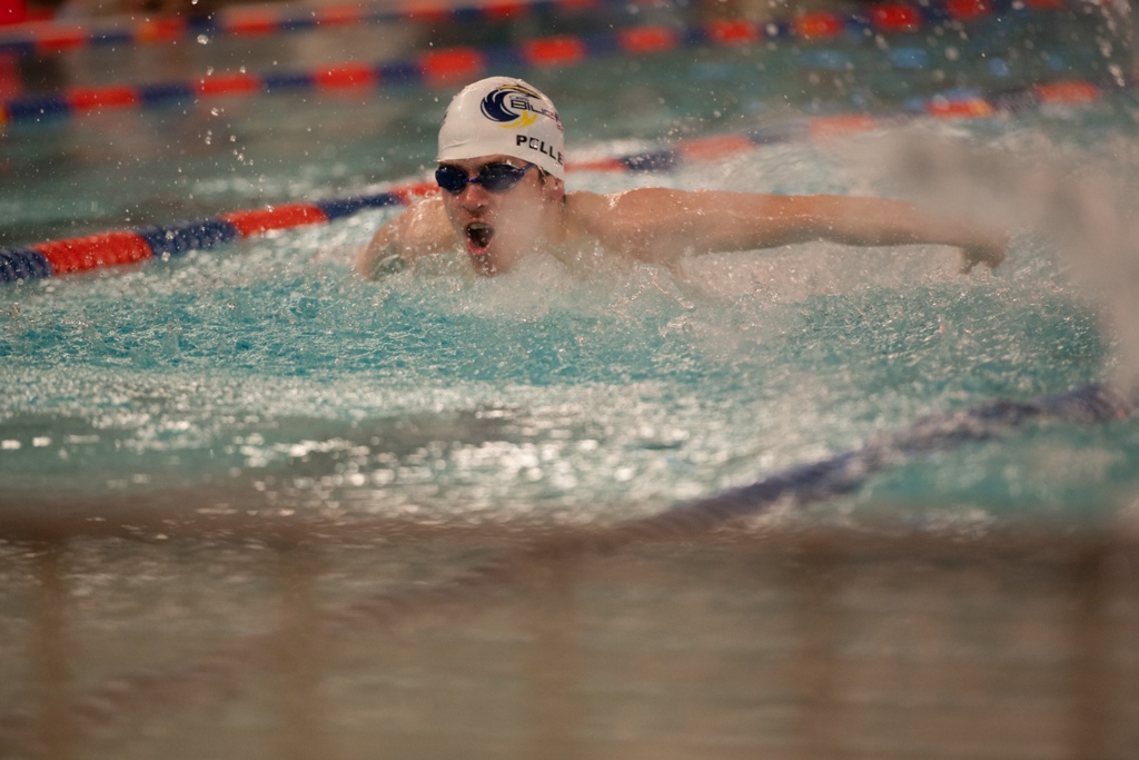 An action shot photo of a swimming athlete in the water. The athlete is wearing black goggles and a white swim cap.