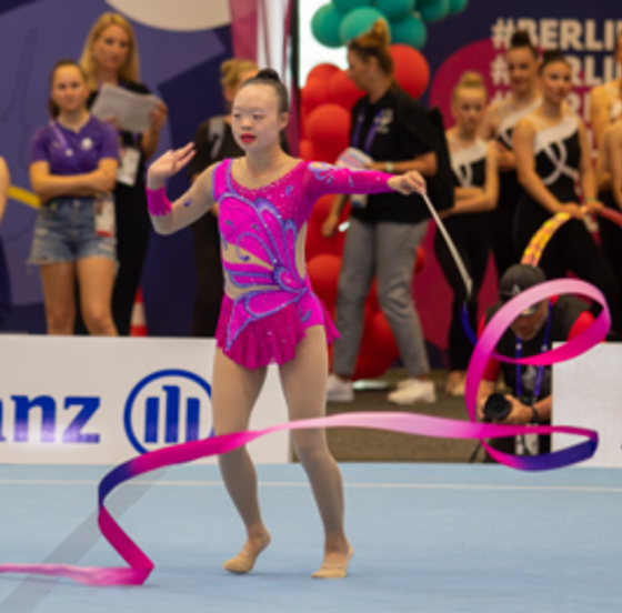 Girl in a purple bodysuit with a rhythmic gymnastics baton.