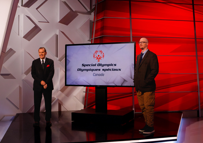 Two men standing, both are wearing suits. Between them is a TV screen with the Special Olympics Canada logo.