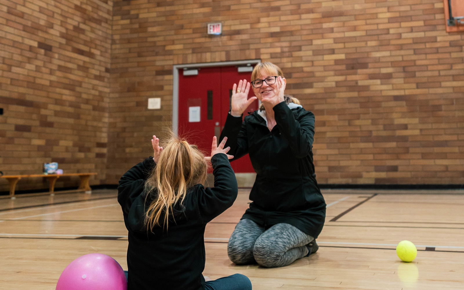 A young girl with her back to the camera is making gestures with her hands in play with her mom who sits opposite her.