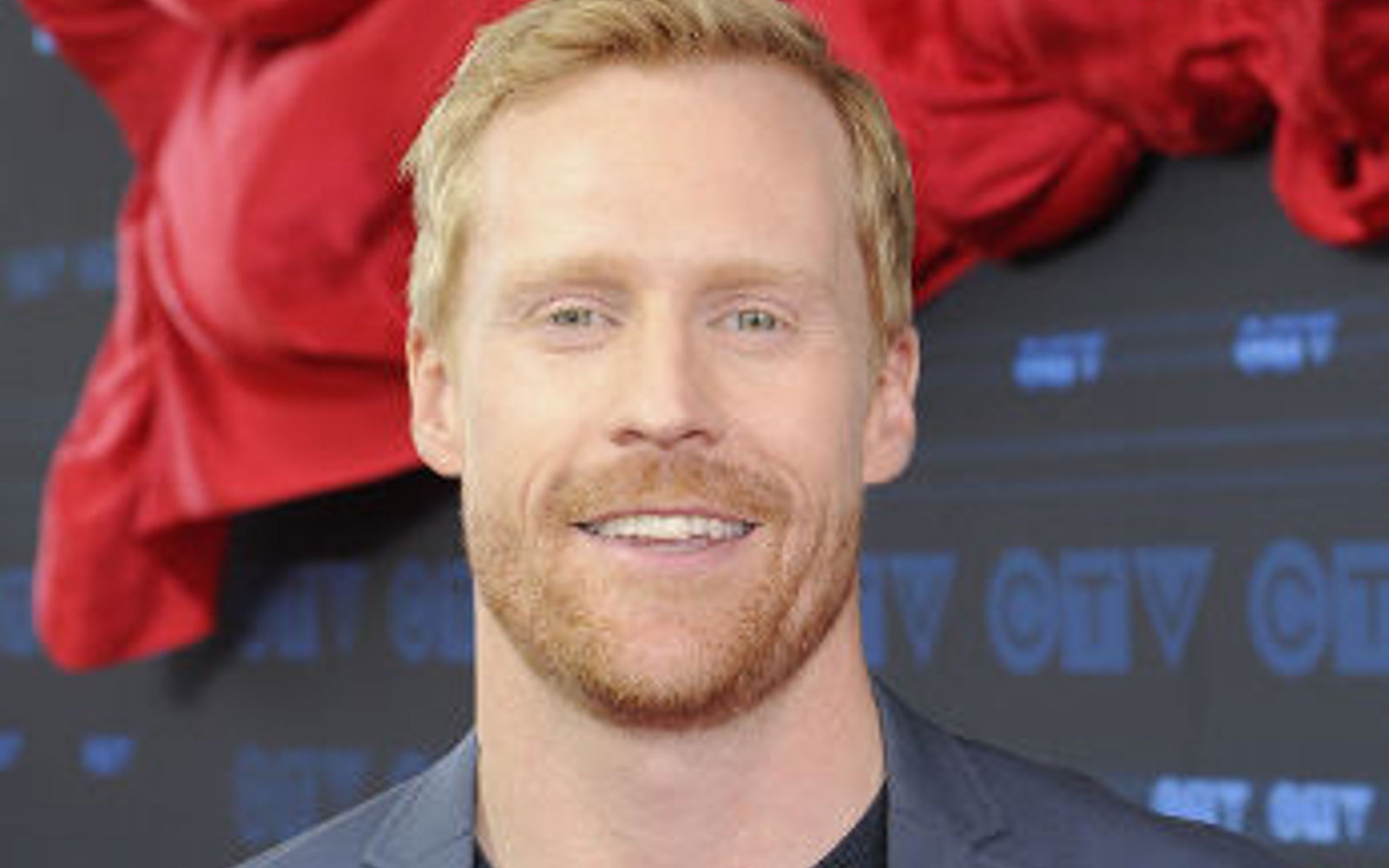 Portrait d'un homme vêtu d'un t-shirt noir et d'un blazer gris.