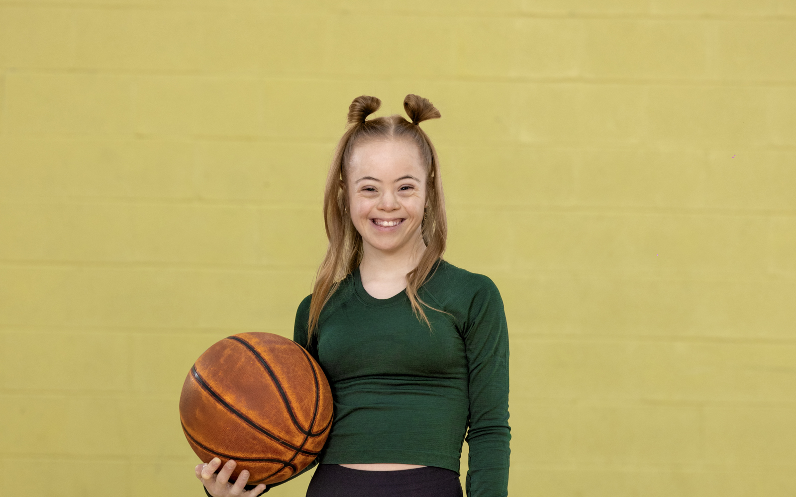 Jeune femme en chemise verte et pantalon noir tenant un ballon de basket
