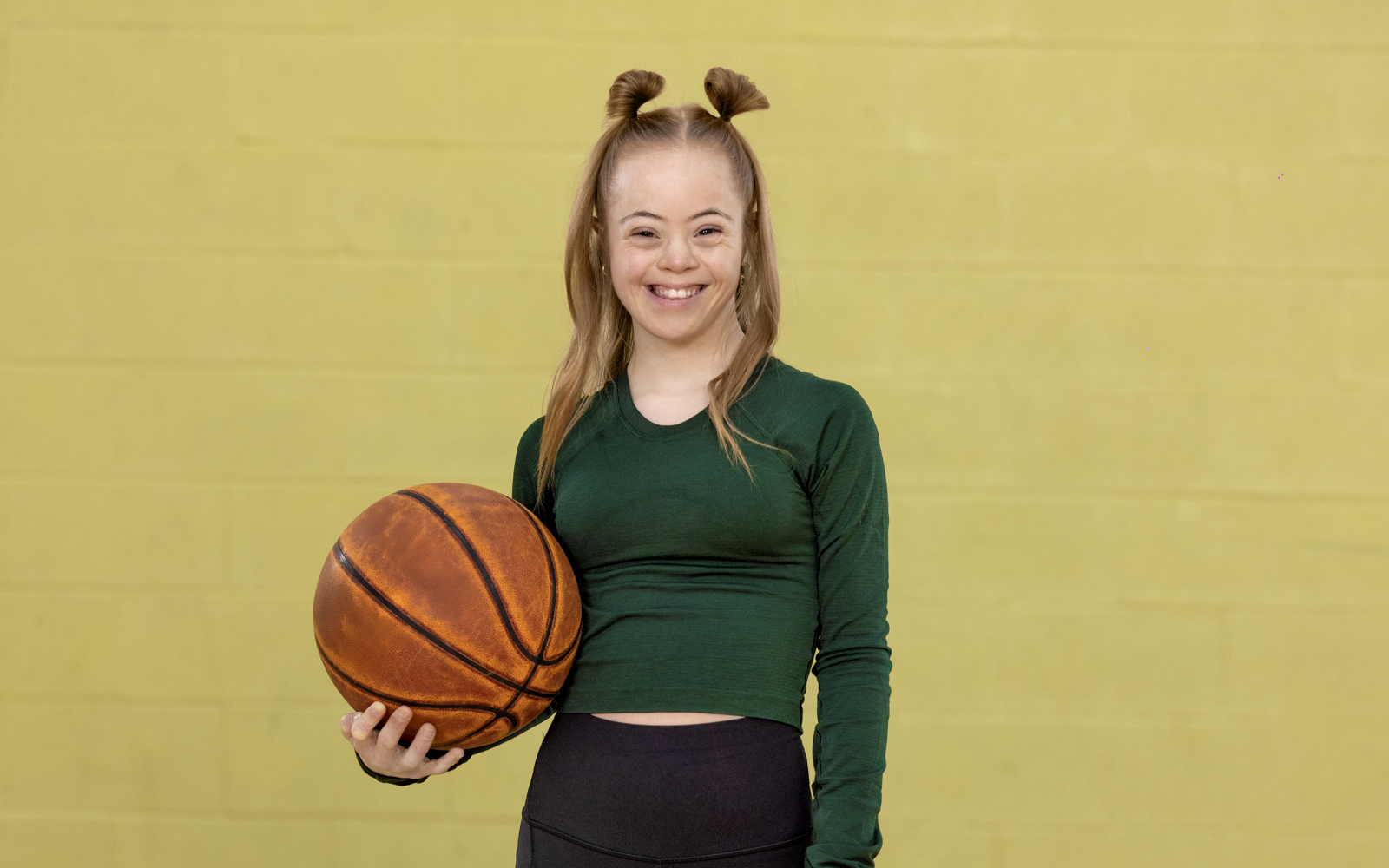 Young woman in green shirt and black pants holding a basketball