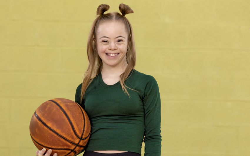 Jeune femme en chemise verte et pantalon noir tenant un ballon de basket