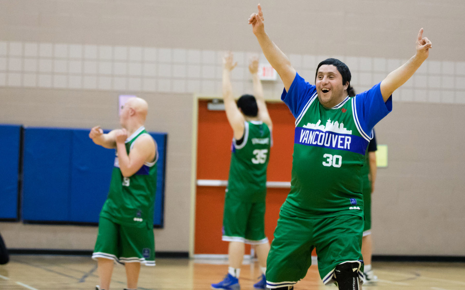 Special Olympics BC basketball athlete raises his hands in their air after winning the game.