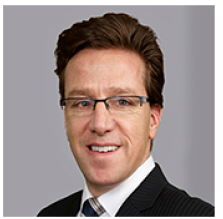 Man in black suit with white shirt and dark hair smiling at the camera. 