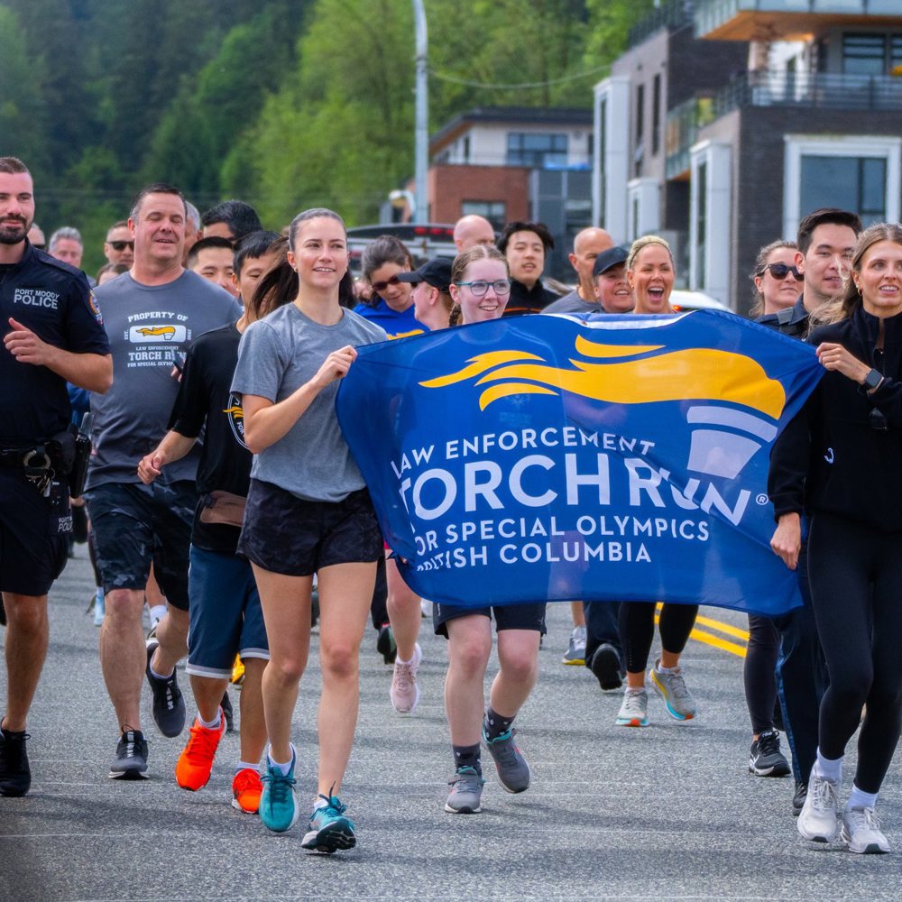 A group of participants run together holding a banner at the Port Moody Police Department Law Enforcement Torch Run Torch Run event.