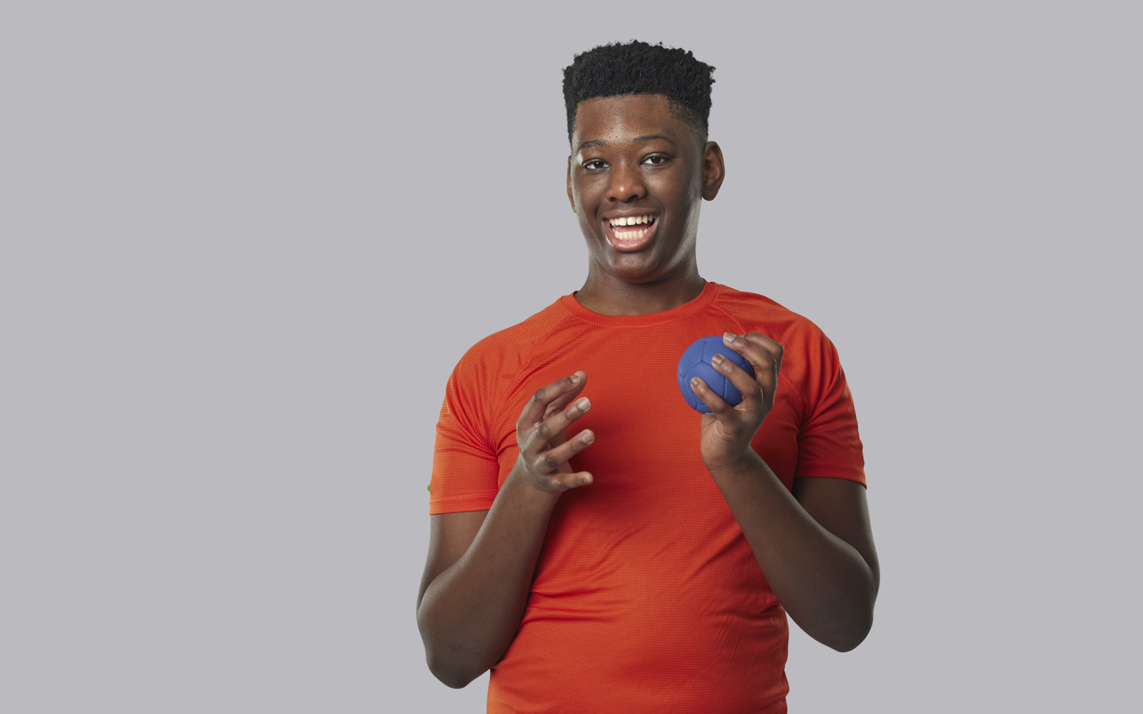 Young Boy in an orange shirt holding a small blue ball 