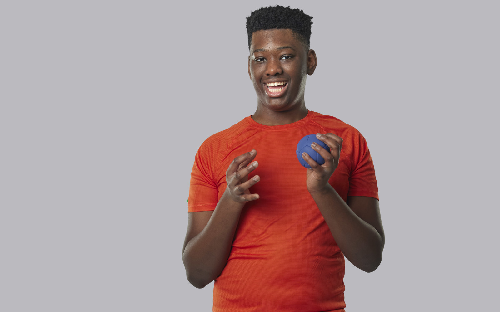 Jeune garçon en chemise orange tenant une petite balle bleue