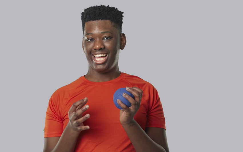 Young Boy in an orange shirt holding a small blue ball 