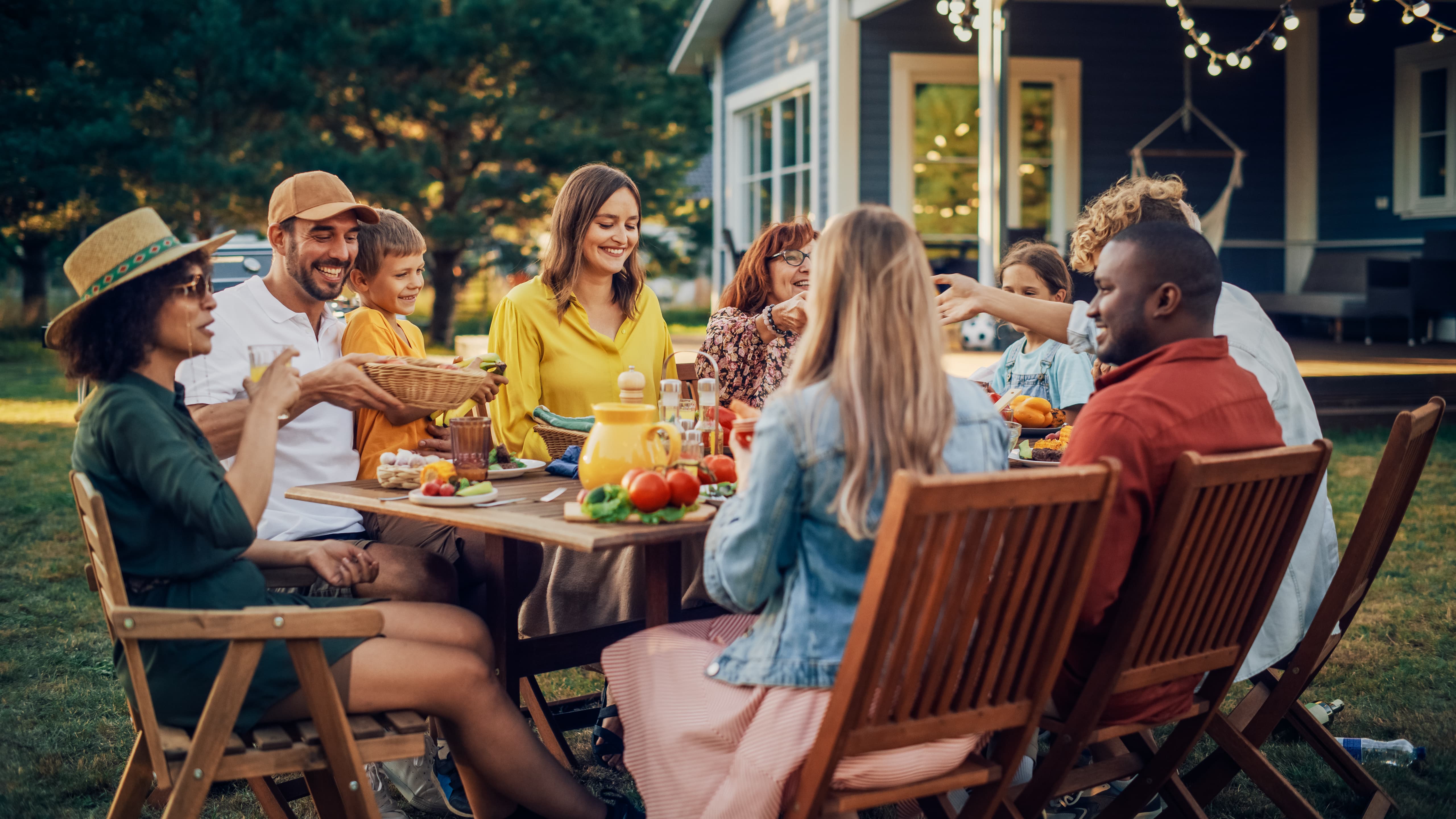 Group of people sitting outside at a picnic table, with table covered in food and drinks. Group of people sitting outside at a picnic table, with table covered in food and drinks.