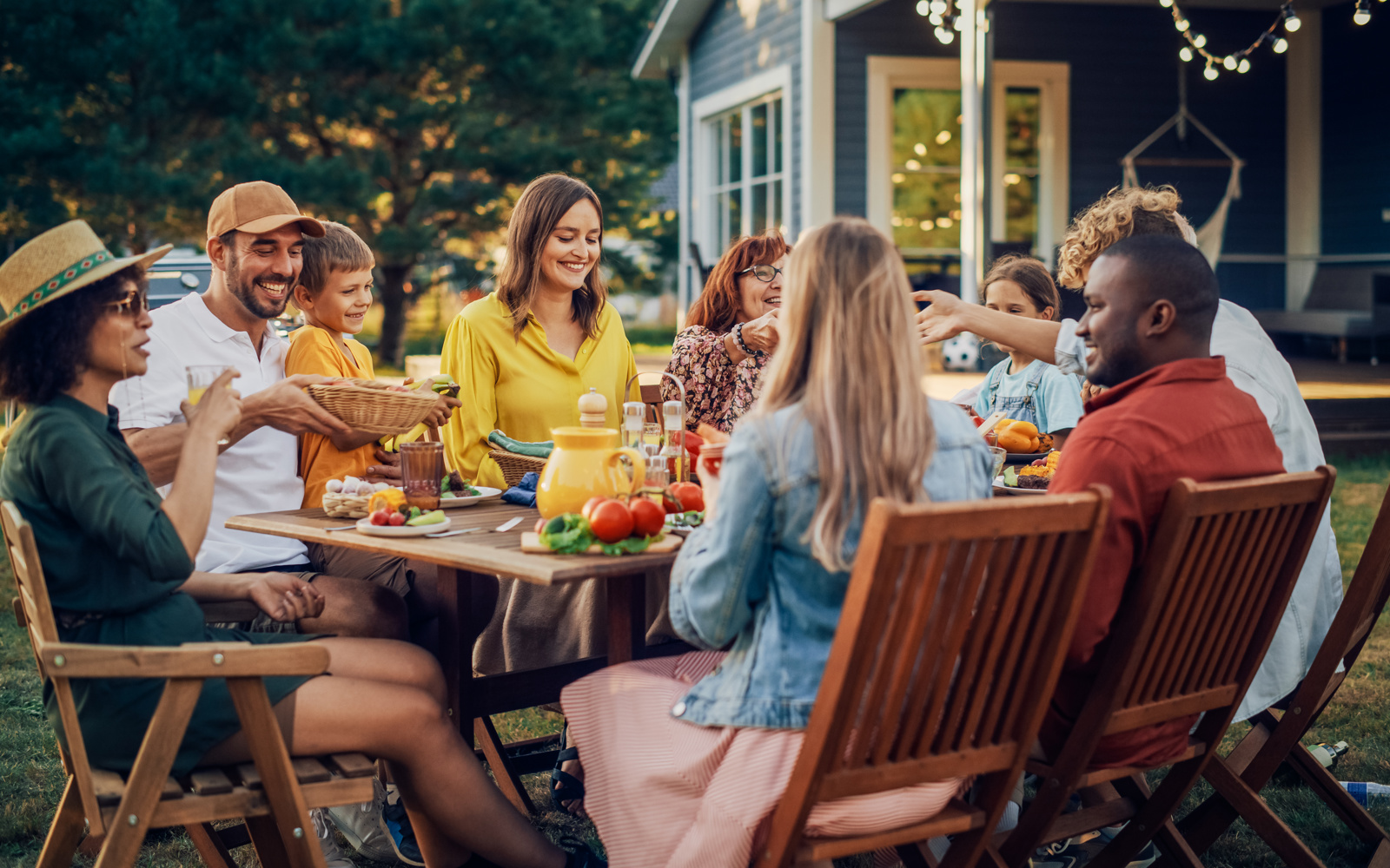 Group of people sitting outside at a picnic table, with table covered in food and drinks. 