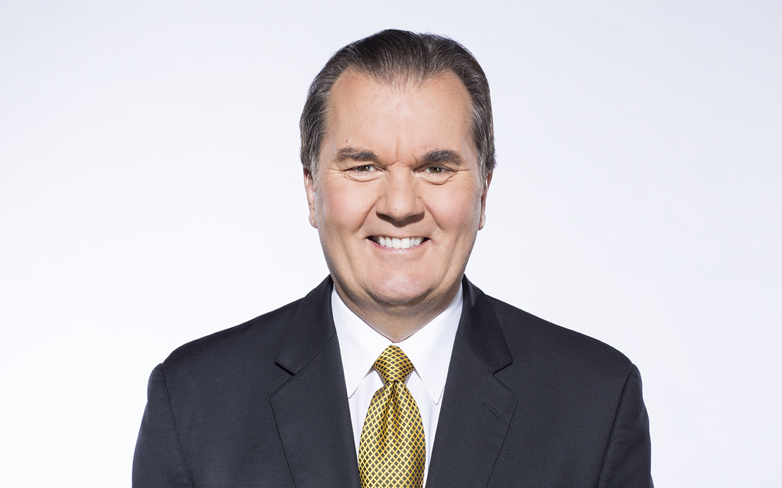 Portrait d'un homme vêtu d'un blazer noir, d'une chemise blanche et d'une cravate jaune et noire.