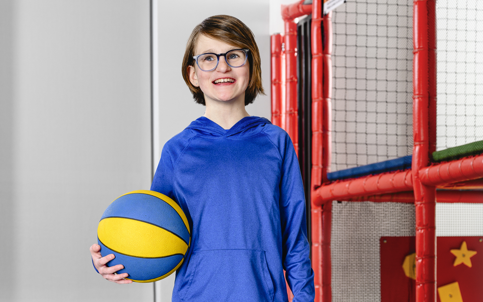 Young girl in blue shirt holding a blue and yellow ball 