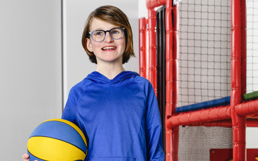 Young girl in blue shirt holding a blue and yellow ball