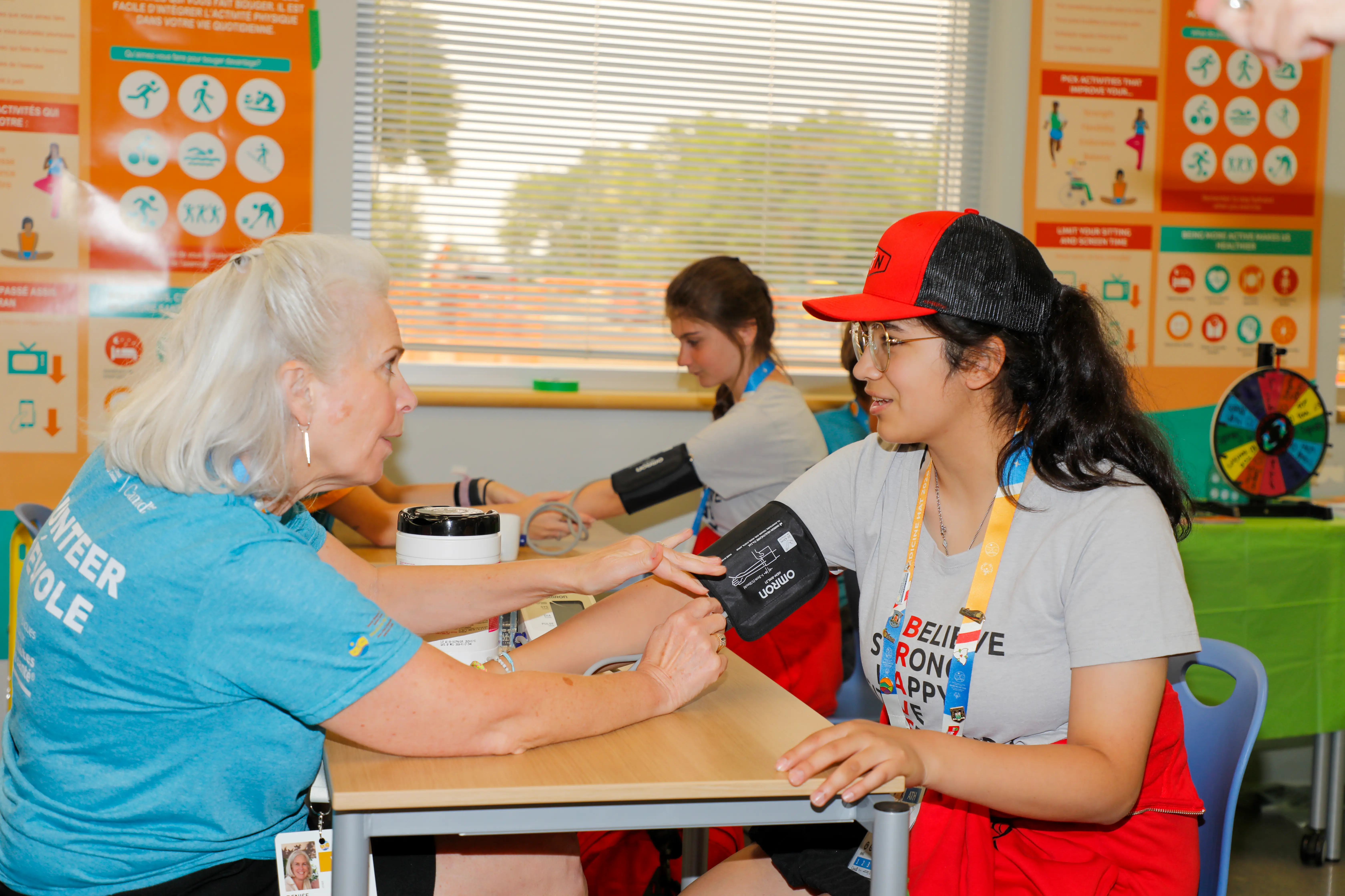 A Special Olympics Canada athlete getting her blood pressure taken by one of the Healthy Athletes volunteers. They are both sitting at a table and deep in conversation. A Special Olympics Canada athlete getting her blood pressure taken by one of the Healthy Athletes volunteers. They are both sitting at a table and deep in conversation.