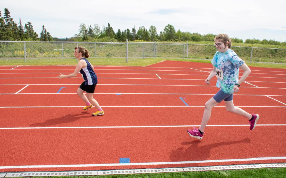 An action shot photo of two athletes running on the track. The photo was taken from the side of the athletes so it looks as if they are running from right to left.