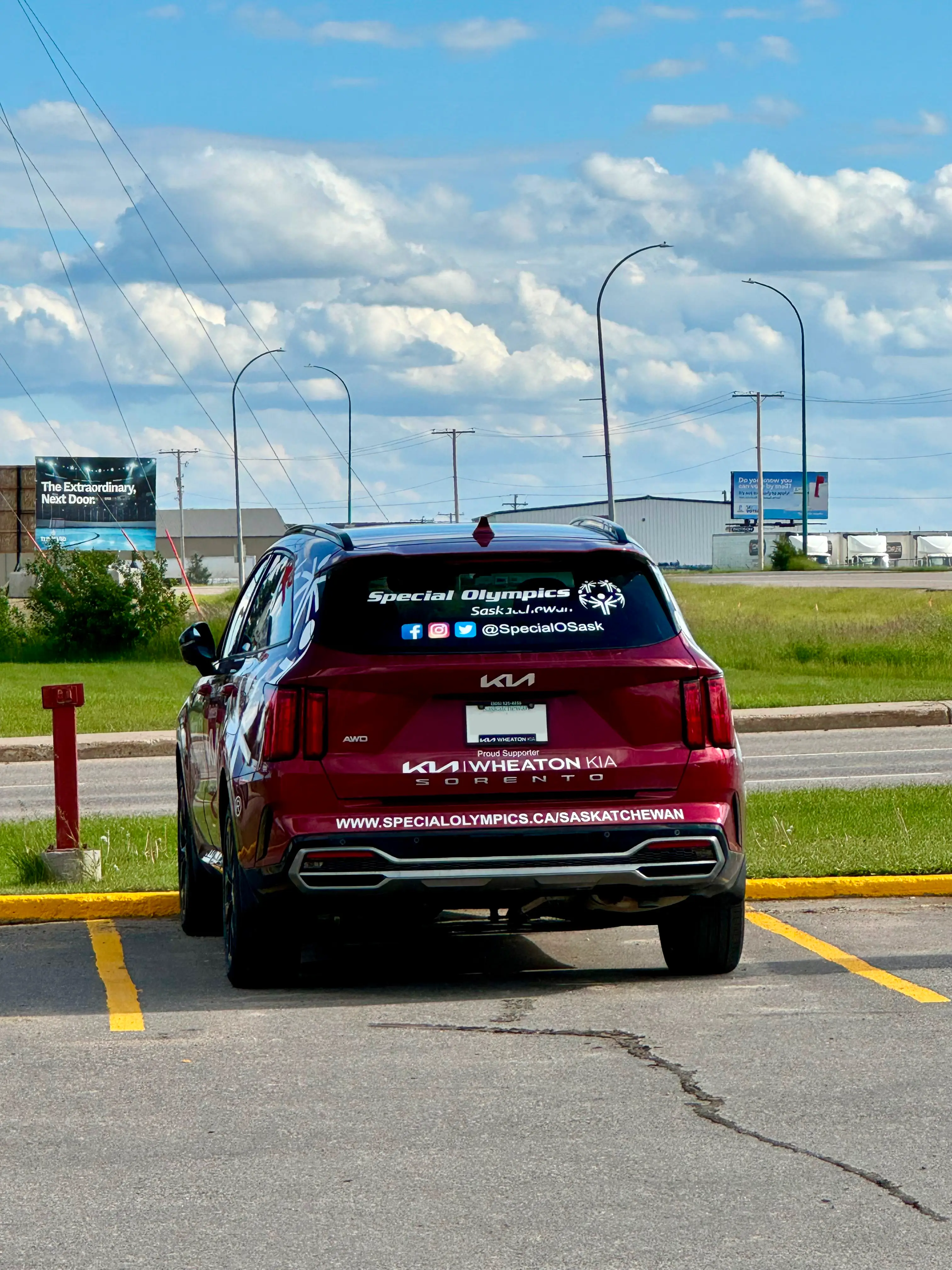 A red Kia car is parked in a parking spot. The car has the Special Olympics Saskatchewan logo on the window along with the social media icons and social media handle in white letters. Also in white letters and written along the bottom of the car is Special Olympics Saskatchewan's website. A red Kia car is parked in a parking spot. The car has the Special Olympics Saskatchewan logo on the window along with the social media icons and social media handle in white letters. Also in white letters and written along the bottom of the car is Special Olympics Saskatchewan's website.