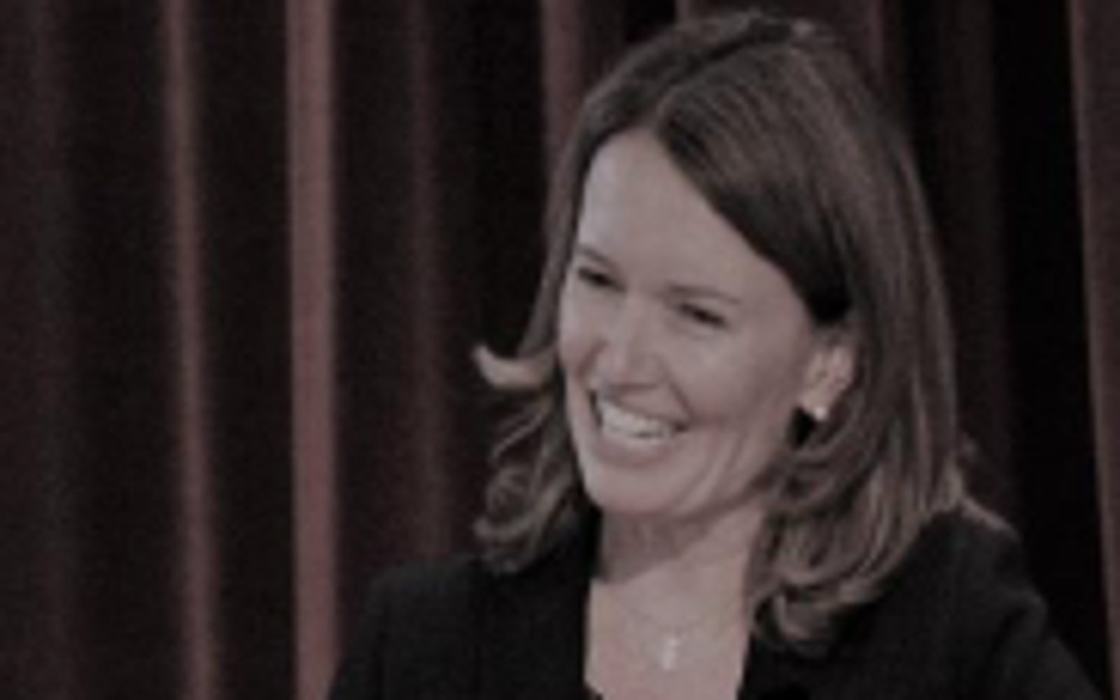 Femme aux longs cheveux noirs et portant un pull noir souriant à l'appareil photo.