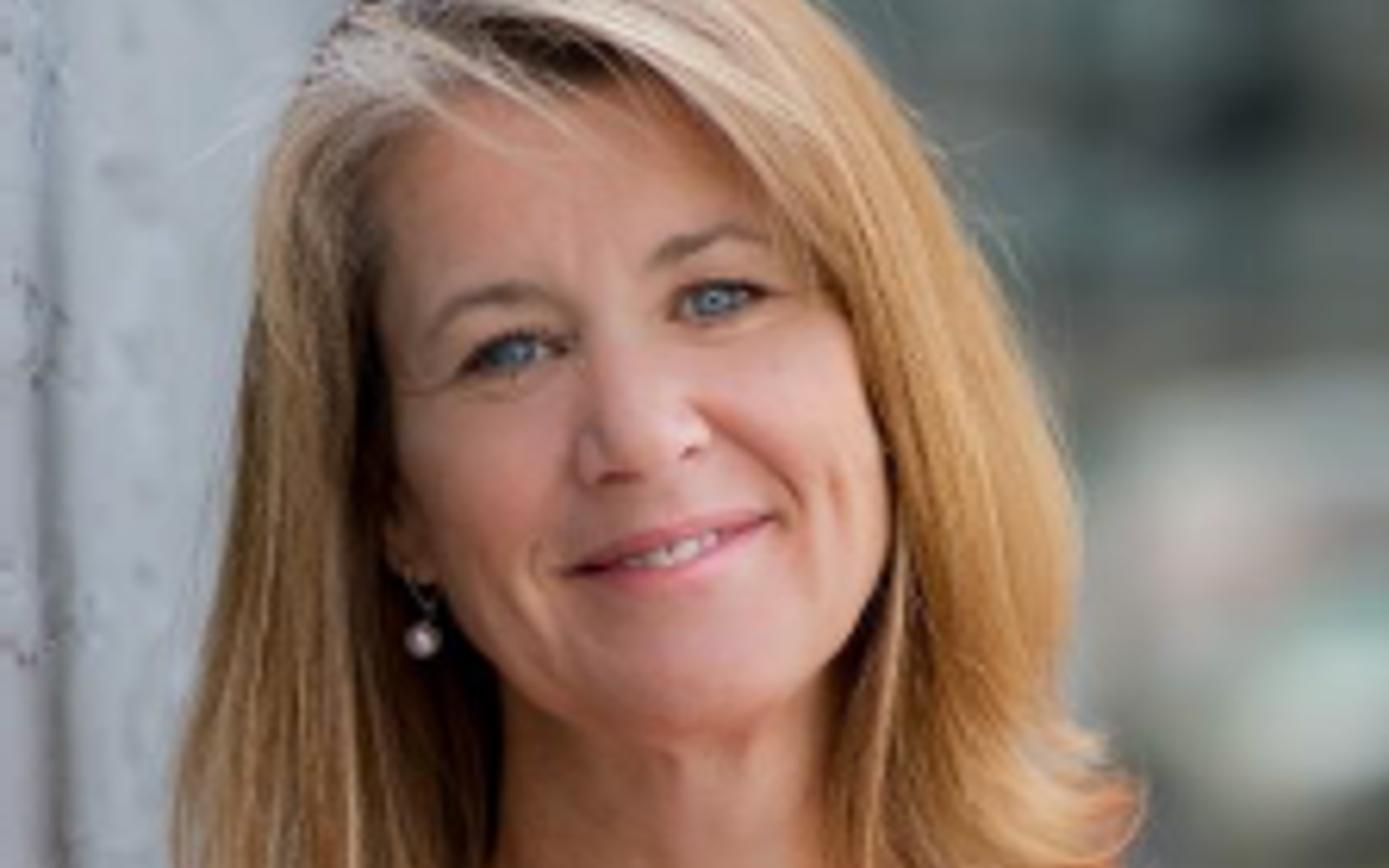 Women with long blond hair and bright orange sweater with pearls.