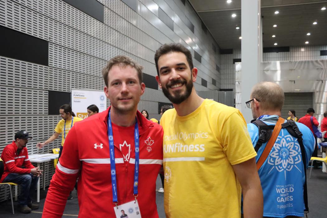 Deux hommes se tiennent côte à côte et regardent fixement la caméra. L'un porte l'uniforme de l'équipe canadienne des Jeux olympiques spéciaux, l'autre un t-shirt jaune FUNFitness. 