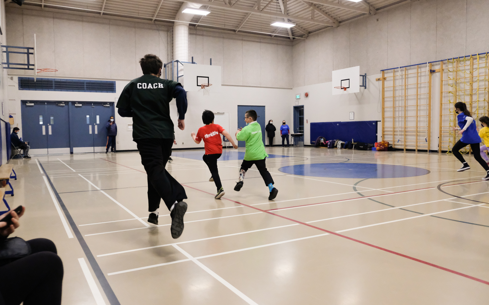 Youth athletes run across a gymnasium with their coach in Surrey.