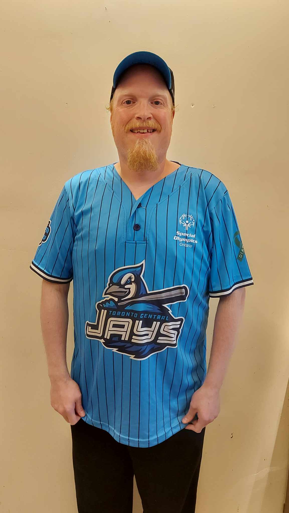 Man in a blue jays jersey and a hat smiles at the camera 
