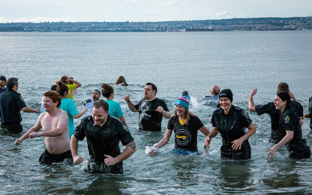 A large group of Law Enforcement Torch Run Polar Plunge participants wade out of the frigid waters with smiles on their faces.
