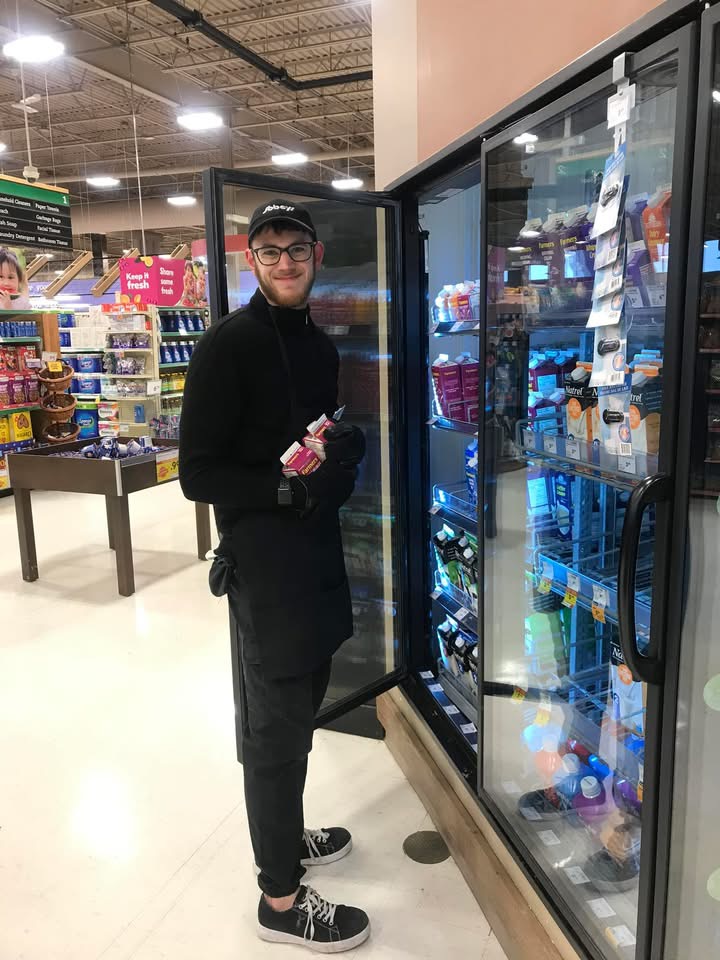 Maxim Thibault, SO athlete and Sobey's employee, stocking a freezer in a grocery stock wearing work attire. 
