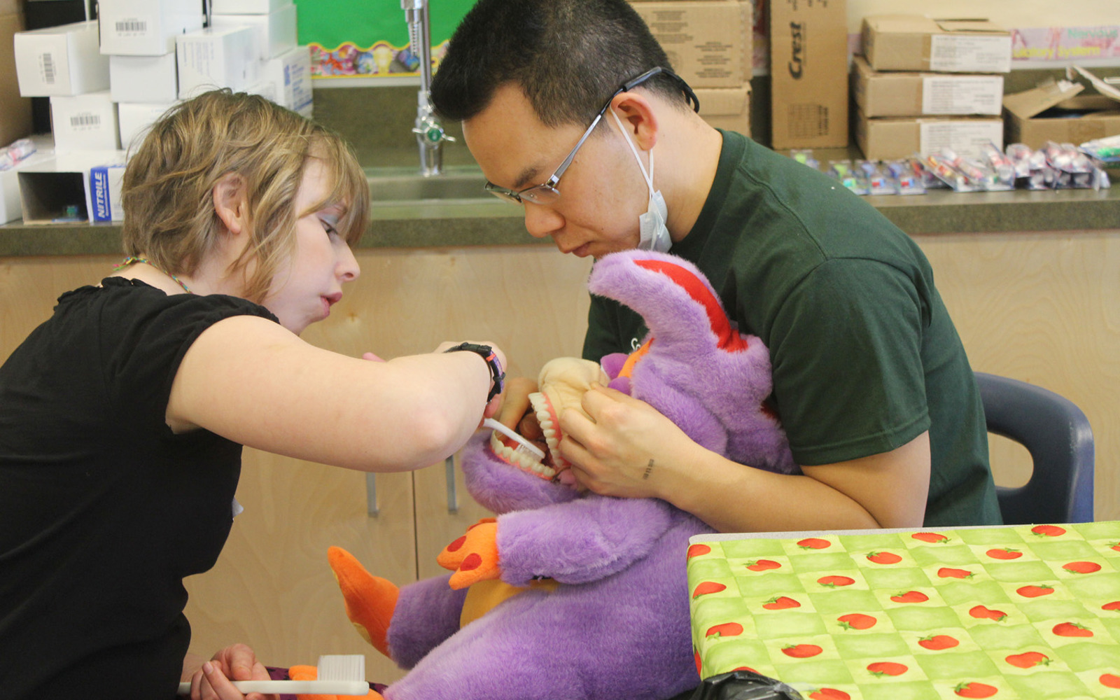 At a Special Smiles event, a volunteer holds a stuffed animal's mouth open so a young girl can practice brushing them. 