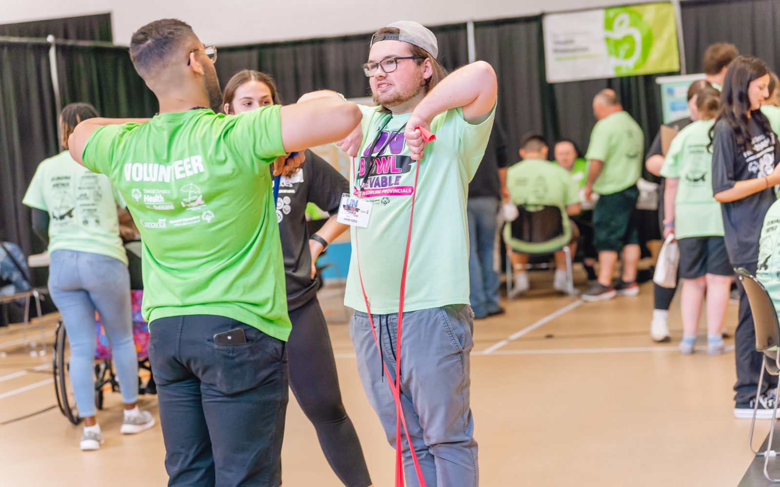 Two people standing using a tension band to workout.