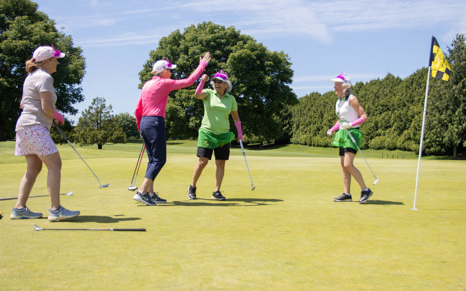 A foursome of ladies dressed in fun costumes gives a high-five after a successful putt on the golf greens. 