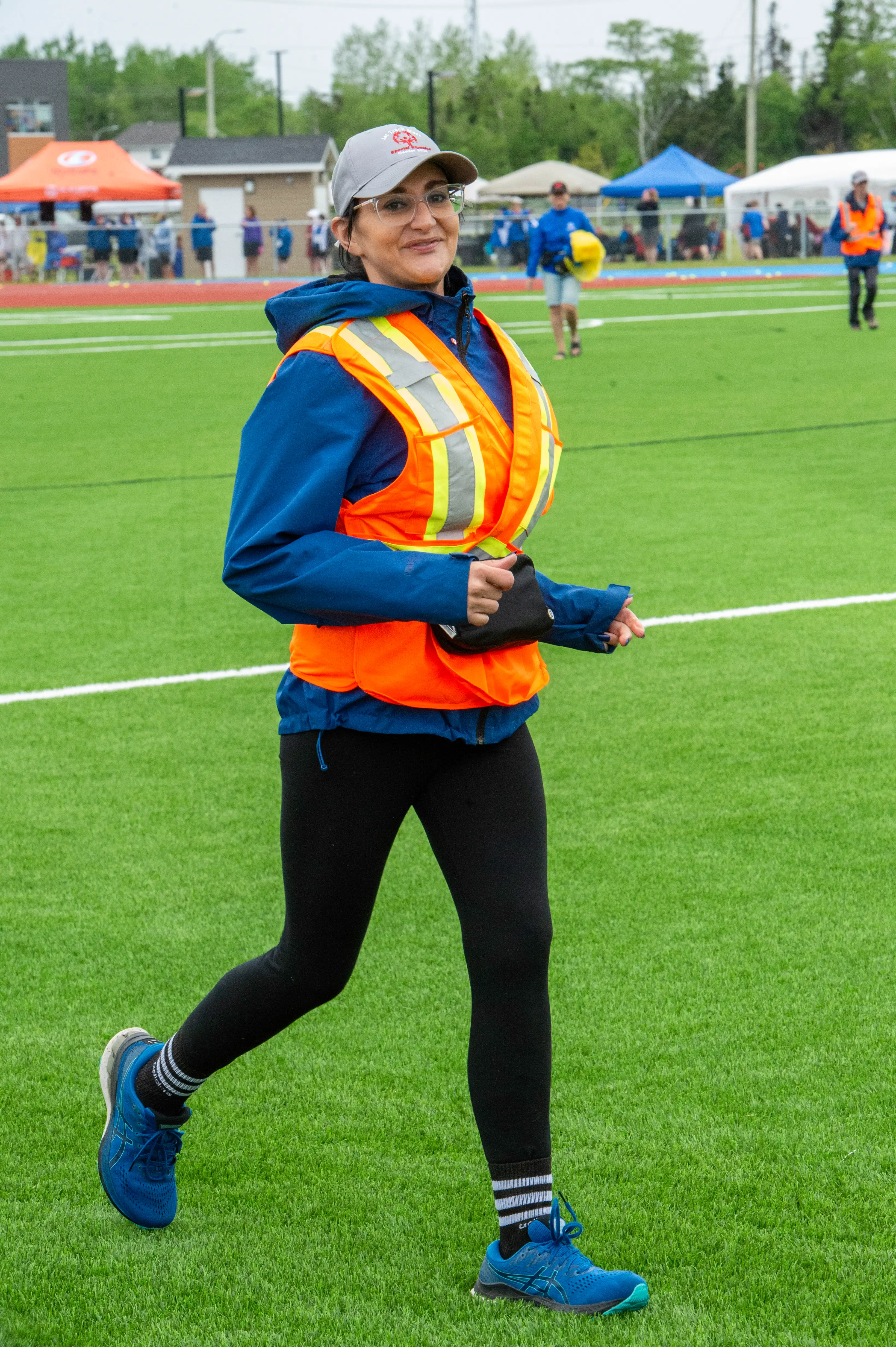 A photo of a volunteer mid run, wearing a bright orange and yellow safety vest, and a Special Olympics Newfoundland & Labrador grey baseball cap. A photo of a volunteer mid run, wearing a bright orange and yellow safety vest, and a Special Olympics Newfoundland & Labrador grey baseball cap.